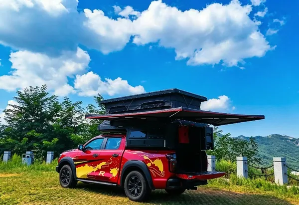 Red pickup with the slide-in camper and awning open in the mountains