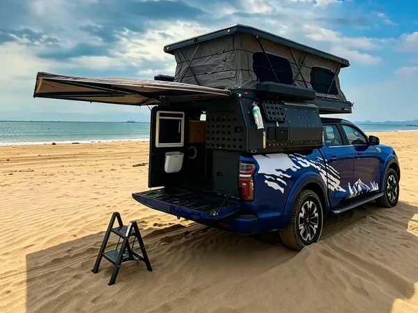 Blue pickup with the slide-in camper open and awning out on a sandy beach
