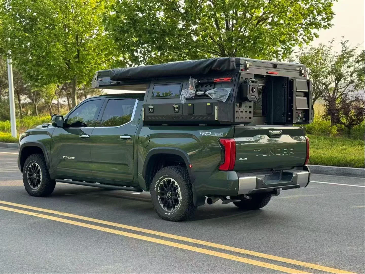 Green Toyota Tundra with a SUNHOMEE slide-in camper on a tree-lined road