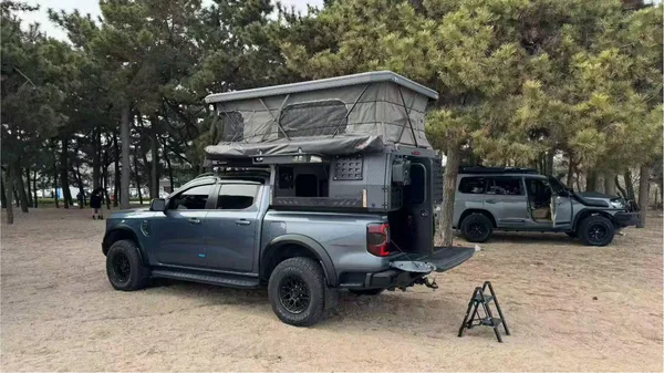 Grey pickup with a slide-in camper at a pine-forest campsite, tailgate and step down