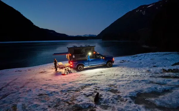 Slide-in camper lit up at night on a snowy lakeshore