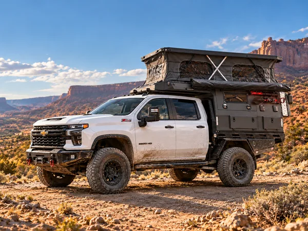 White Chevrolet Silverado 2500HD with a SUNHOMEE flatbed camper in desert canyon country