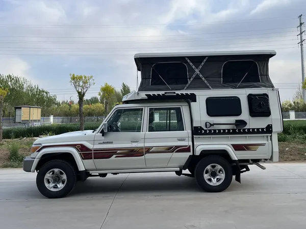 White Toyota Land Cruiser 79 with a SUNHOMEE tray-mount camper, pop-up roof raised, side view