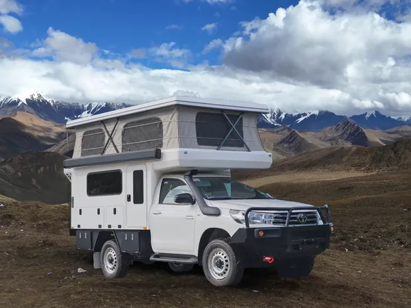 SUNHOMEE tray-mount camper with the pop-up roof raised on a Toyota Hilux cab-chassis, Tibetan mountains behind