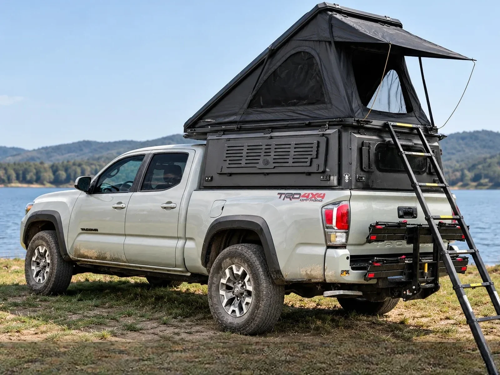 Integrated pop-up topper open on a white Toyota Tacoma by a lake
