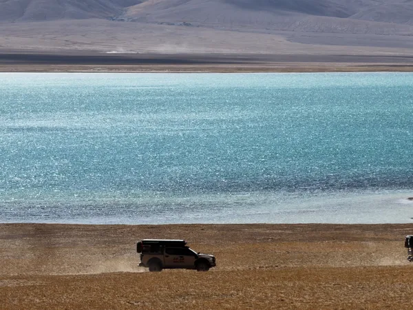 Camper trucks driving along a turquoise high-altitude lake