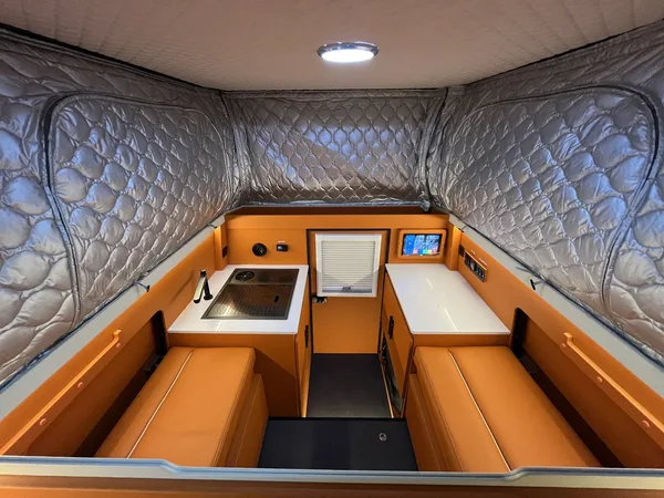Orange camper interior with dinette benches, sink and fridge